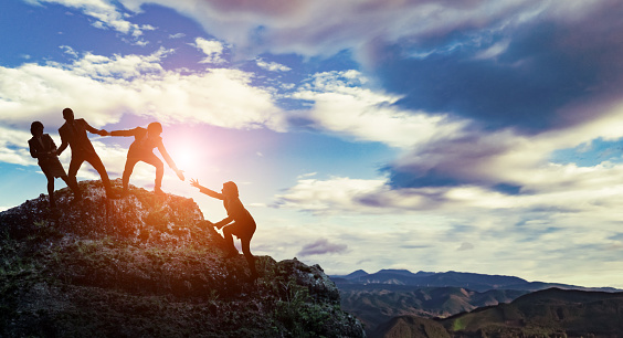 Group of people climbing a mountain helping each other