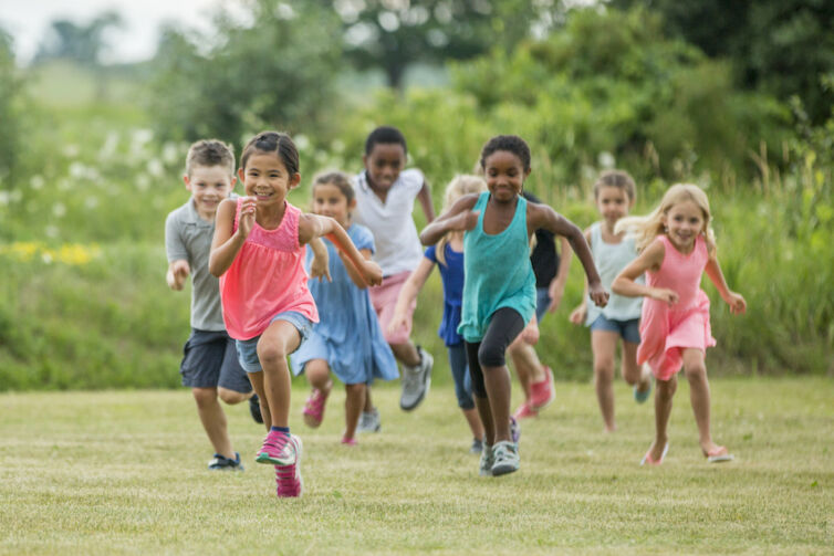 A multi-ethnic group of elementary age children are playing together outside at recess. They are chasing each other and are playing tag.