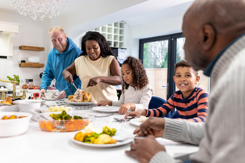 A multigeneration family preparing freshly cooked food with each other. They are all wearing casual clothing and having a lovely afternoon.